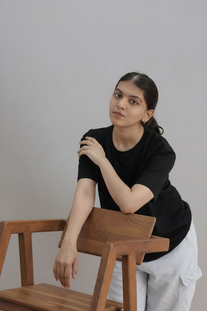 Woman sitting on a wooden stool against a plain background