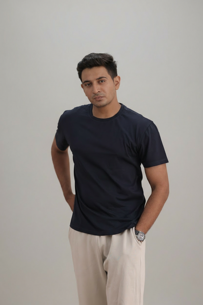 Man wearing a navy blue t-shirt and cream pants against a plain background