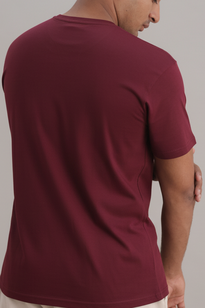 Man wearing a maroon t-shirt and beige pants against a plain background