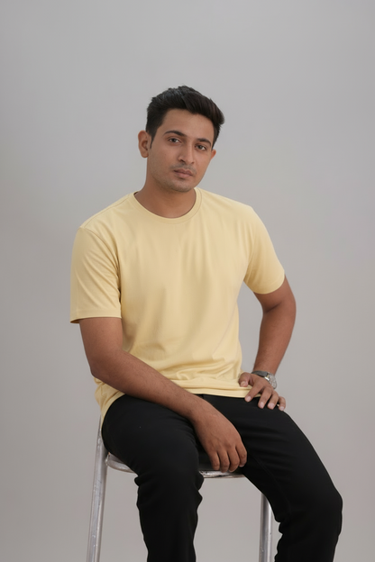Man sitting on a stool wearing a yellow t-shirt and black pants against a gray background